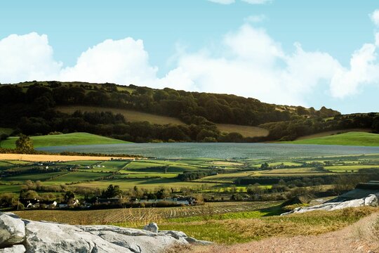 Fototapeta Flat design scene showing hedged farm plots, farmhouses, reservoir, wooded hills, rocky outcrop