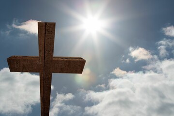 Rough wooden cross is rising in flat design against bright blue sky with lens flare, clouds