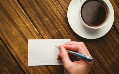 Cropped hand writing on paper at desk with coffee cup