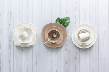 Top view of modern ceramic tableware arrangement featuring off-white and beige dishes with matching...