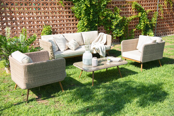 Outdoor patio setup with woven rattan sofa and armchairs in beige tones, decorative cushions, throw...