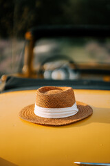 Straw hat resting on a classic yellow convertible during a sunny day outdoors