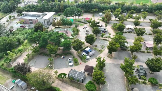 Drone aerial view of a family-friendly campground with playground, RVs, tents and picnic zones surrounded by trees