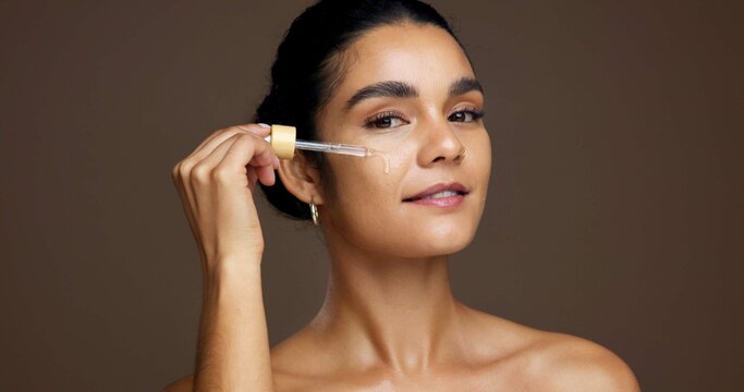 Beauty, portrait and serum with woman in studio for antiaging cosmetics or dermatology treatment. Aesthetic, dropper and smile of model on brown background to apply liquid skincare product to face