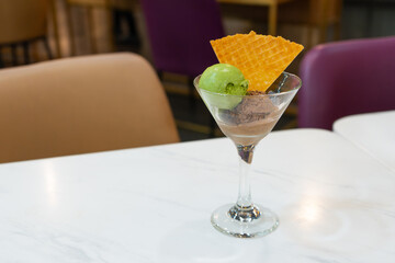 Assorted scoops of ice cream with matcha and chocolate flavours, served in a transparent glass, put on white table, in a cafe environment