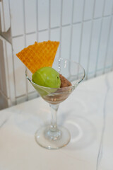 Assorted scoops of ice cream with matcha and chocolate flavours, served in a transparent glass, put on white table, in a cafe environment