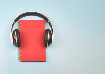 red  diary or planner covered with headphones on blue background  with copy space. , Audio book.