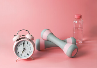 pink vintage alarm clock,  gray pink dumbbells and  bottle of water on pink background with copy space. Self development and active lifestyle.