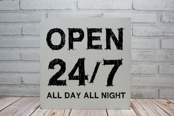 Open 24/7 All Day All Night sign with blackboard on white brick background