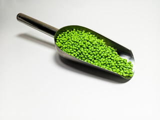 Green plastic masterbatch, polymer carries colorful pigments with small scoops poured into a white background, suitable for product catalog design of industrial plastic manufacturing company profiles