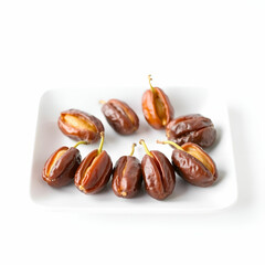 Obraz premium Pile of ripe dates on a white plate isolated on white background. Sweet dried fruit dessert snack. Healthy food source of vitamins. Vegetarian nutrition.