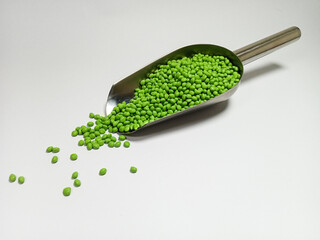 Green plastic masterbatch, polymer carries colorful pigments with small scoops poured into a white background, suitable for product catalog design of industrial plastic manufacturing company profiles
