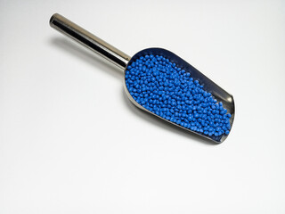 Blue plastic masterbatch, polymer carries colorful pigments with small scoops poured into a white background, suitable for product catalog design of industrial plastic manufacturing company profiles