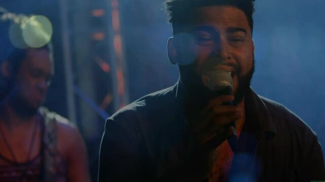 Lead vocalist stepping into spotlight and singing into mic over guitar rhythms to express emotion