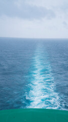 A long, straight wake trails behind a boat, cutting through the calm, blue expanse of the ocean...