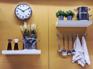 Organized kitchen wall featuring clock, shelves, utensils, pots, plants, and neatly folded towels