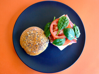 A cold Danish salami burger with cheese, tomato and spinach leaves on a brioche bun with seeds. 