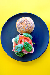 A cold Danish salami burger with cheese, tomato and spinach leaves on a brioche bun with seeds. 