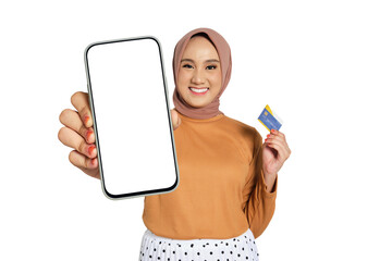 Smiling woman wearing hijab showing blank smartphone screen and holding credit card isolated on...