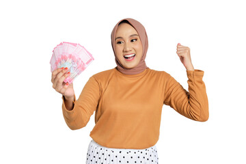 Happy young Muslim woman in hijab holding Indonesian rupiah money and celebrating success isolated...