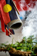 An Indigenous smoking ceremony showing native leaves on fire and smoking, an aboriginal flag and a...