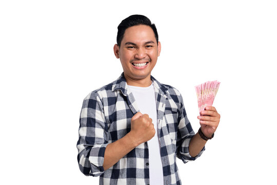 Happy young man in checkered shirt holding Indonesian rupiah money and celebrating success with clenched fist isolated on transparent background