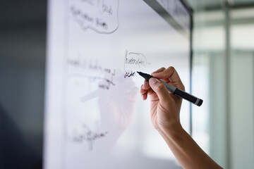 A hand writing on a whiteboard with a black marker in a bright office space