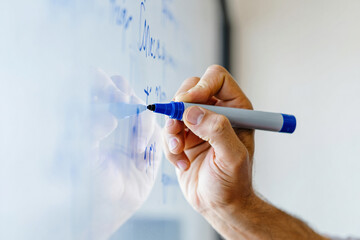 A hand writing on a whiteboard with a blue marker in a close up shot view
