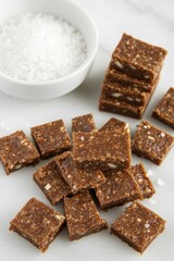 Brown squares, scattered, beside small white bowl of salt