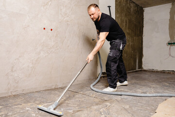Construction worker vacuuming dust and debris after laying tiles in bathroom