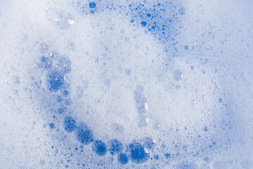 bubbles of detergent foam on blue water. the texture of a soapy cosmetic product. Abstract texture background of whipped white foam. A copy space.