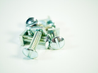 An assortment of shiny metal binding head screws with square nuts resting on a bright white surface...