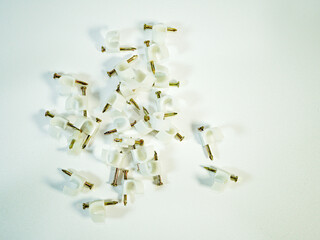 An overhead view displays a collection of white cable clips with brass nails scattered on a bright...