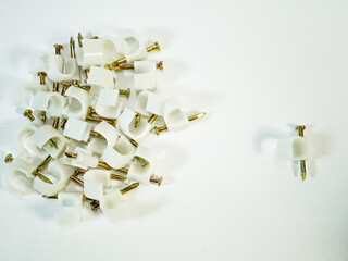 Cable clips with nails scattered on a white surface ready for fastening and organizing wires in...