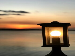 Glowing lantern at sunset with warm blurred background over water