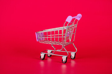 Close up empty toy metal supermarket shopping cart over vivid red background with copy space,