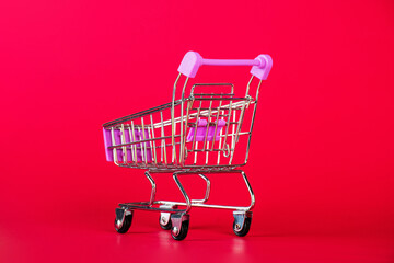 Empty shopping trolley on red background. Space for text.