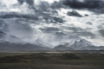 Dramatic landscape panorama of mountain peaks with snow and glaciers in cloudy weather, rays of the sun breaking through the clouds, landscape of the Pamir mountains for the background