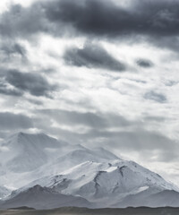 Dramatic landscape panorama of mountain peaks with snow and glaciers in cloudy weather, rays of the sun breaking through the clouds, landscape of the Pamir mountains for the background