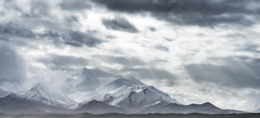 Dramatic landscape panorama of mountain peaks with snow and glaciers in cloudy weather, rays of the...