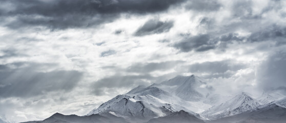 Dramatic landscape panorama of mountain peaks with snow and glaciers in cloudy weather, rays of the...