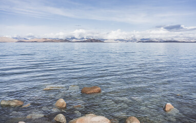 Rocky shore of Lake Karakul and blue water of a high mountain lake against the background of rocky...