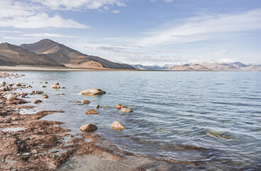 Rocky shore of Lake Karakul and blue water of a high mountain lake against the background of rocky mountain slopes in the Pamirs in the Tien Shan, panoramic landscape for background