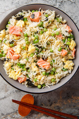 Fried rice with vegetables, salmon, egg and seaweed close-up in bowl on table. Vertical top view from above