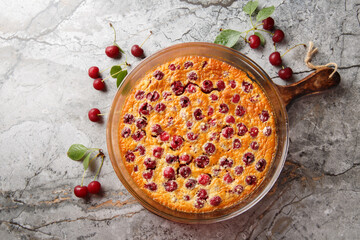 Cherry clafoutis French favorite is a sort of baked custard, studded with fresh cherries, and scented with vanilla close-up in a baking dish on the table. Horizontal top view from above