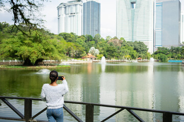 Tourist taking pictures of lake and skyscrapers in kuala lumpur park