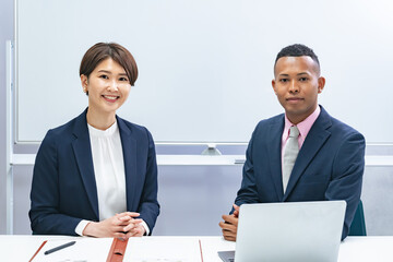A black male businessman and a Japanese female staff member sitting side by side in front of a...