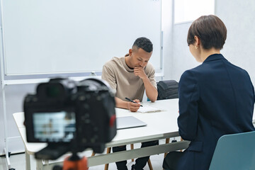 A camera filming a meeting between a black man and a female staff member
