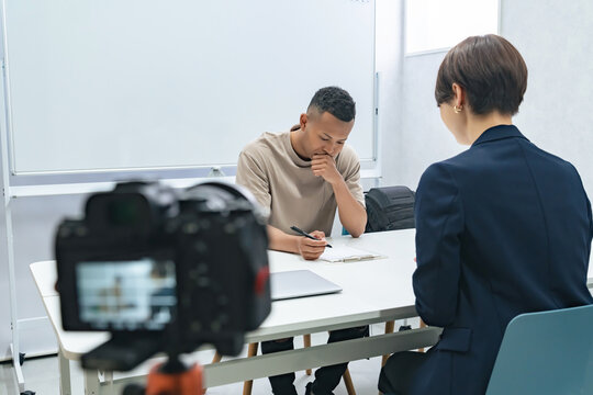A camera filming a meeting between a black man and a female staff member