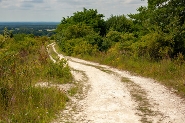 Winding dirt road through lush green hills under a summer sky. Peaceful rural landscape ideal for hiking, biking, or nature escape